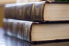 two old books stacked sitting on top of a wooden table